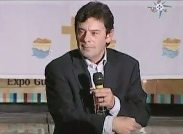 Manuel Capetillo wearing a black suit and long sleeves while holding a microphone.
