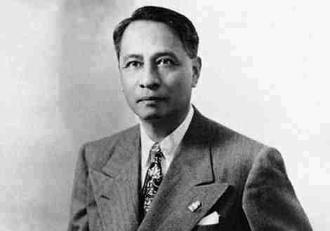 Manuel Roxas with a tight-lipped smile and looking at something while wearing a long sleeve under a necktie and coat with lapel pin and handkerchief