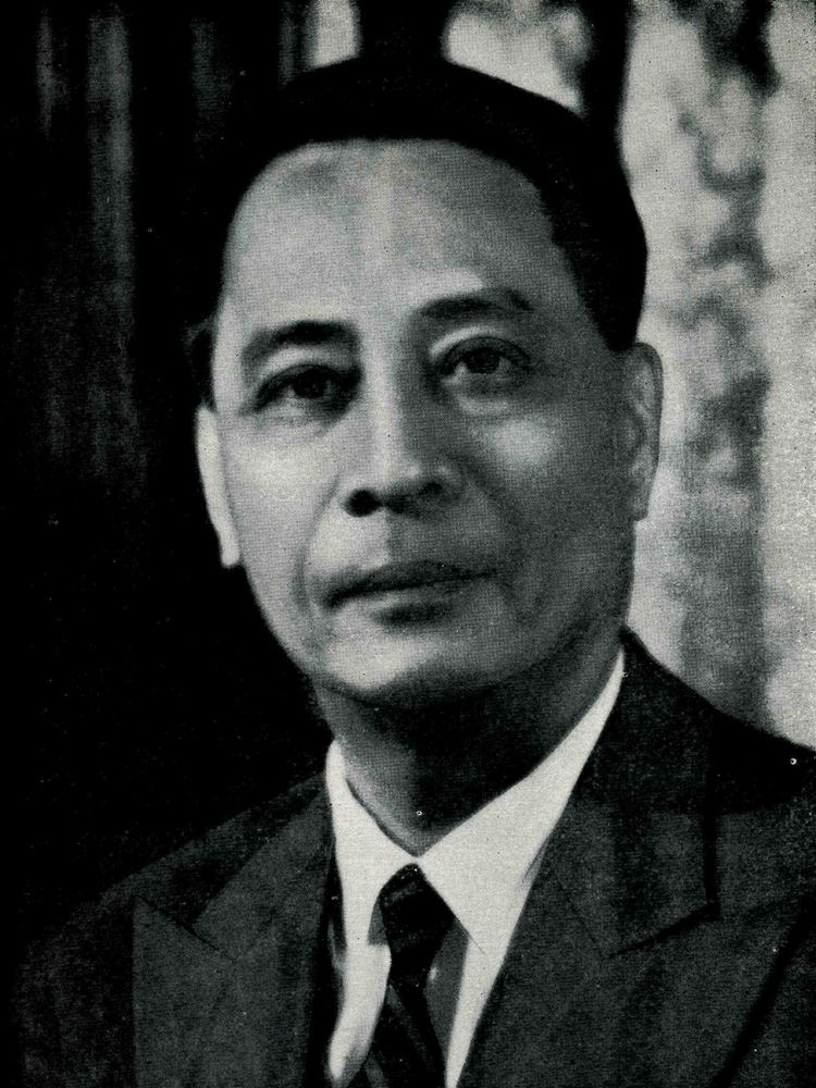 Manuel Roxas with a tight-lipped smile while wearing a long sleeve under a necktie and coat