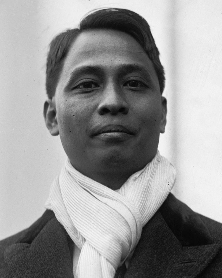 Manuel Roxas with a tight-lipped smile while wearing a trench coat and scarf