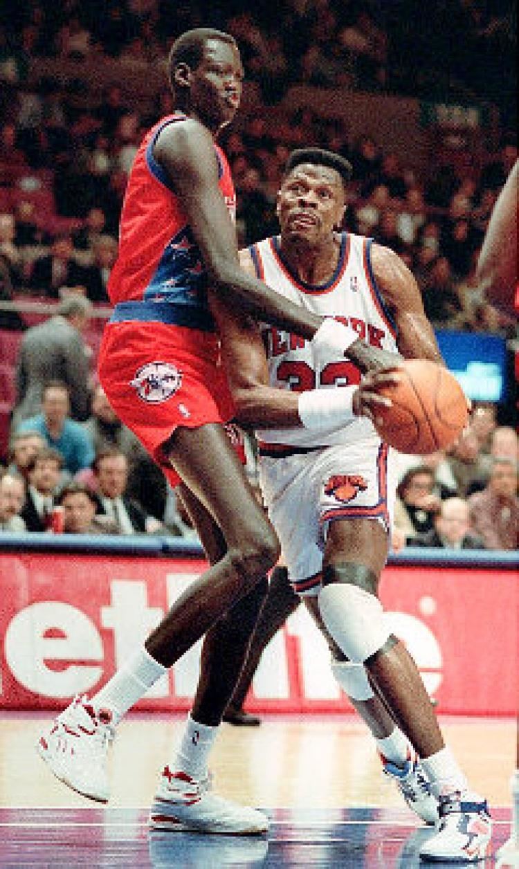 Manute Bol trying to get the ball from the opponent while wearing a red and blue jersey and white and red rubber shoes