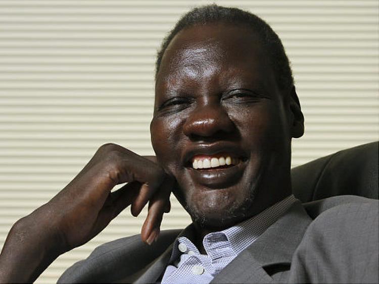 Manute Bol smiling while wearing a gray coat and white and blue long sleeves