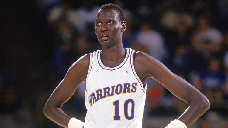 Manute Bol looking afar while hands on his hips and wearing the Warriors jersey with the number 10
