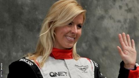 Maria de Villota smiling while waving her hand and wearing a white, black, and red racing suit