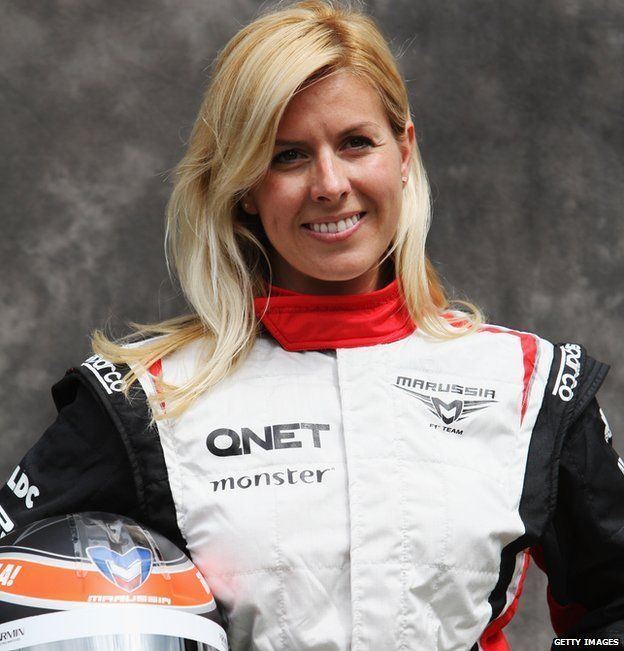 Maria de Villota smiling while holding a helmet and wearing a white, black, and red racing suit
