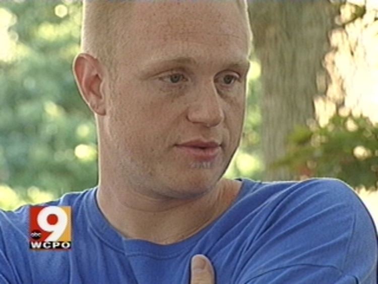 David Carroll is serious, with his hand crossed under his armpit, looking down to his left in 9WCPO news, has white blonde hair, wearing a blue shirt.