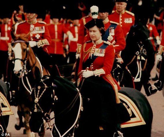 Queen Elizabeth II on horseback as she rode down the Mall in 1981, along with other troops, they are wearing red tunics with medals and bearskin hats