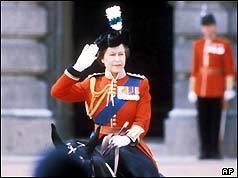 Queen Elizabeth II in a salute gesture is smiling as she rode down the Mall in 1981, and a troop in the background wearing white gloves, red tunics with medals, and bearskin hats