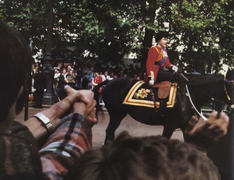 Queen Elizabeth II was on horseback as she rode down the Mall in 1981, with people around her and in the background. Queen Elizabeth is wearing red tunics with medals and bearskin hats