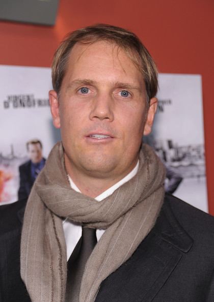 Marcus Thomas wearing brown scarf, black coat, white long sleeves and black neck tie