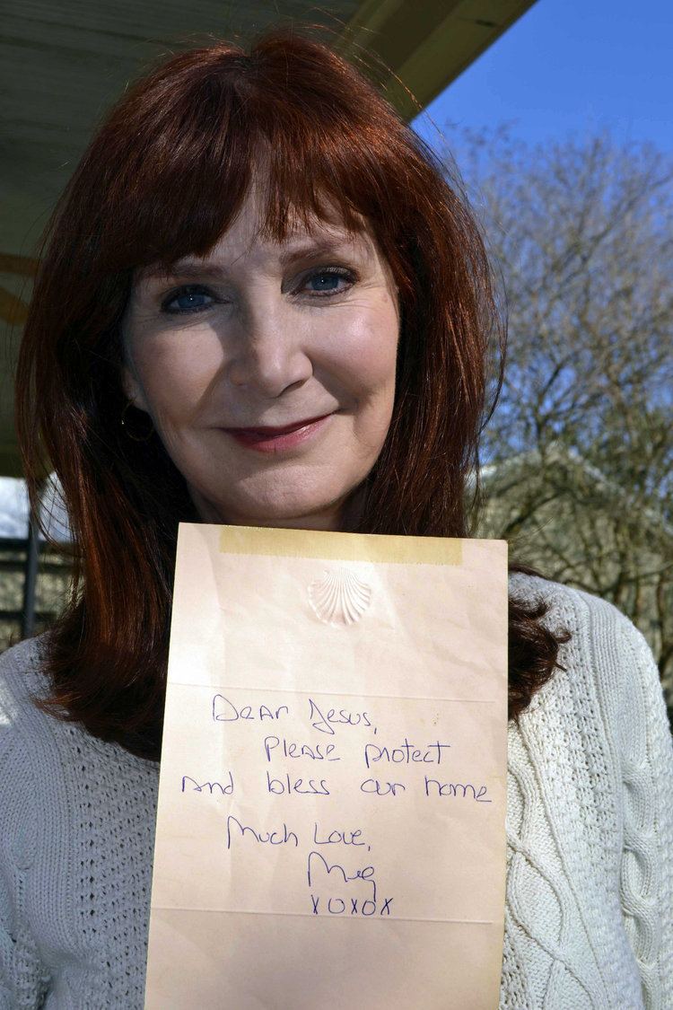 Margaret Orr smiling and holding a letter while wearing a white knitted blouse