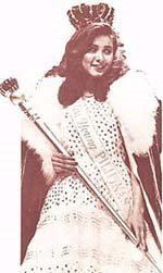 Maria Teresa Carlson smiling while holding a scepter and wearing a crown, gown, sash, and cape