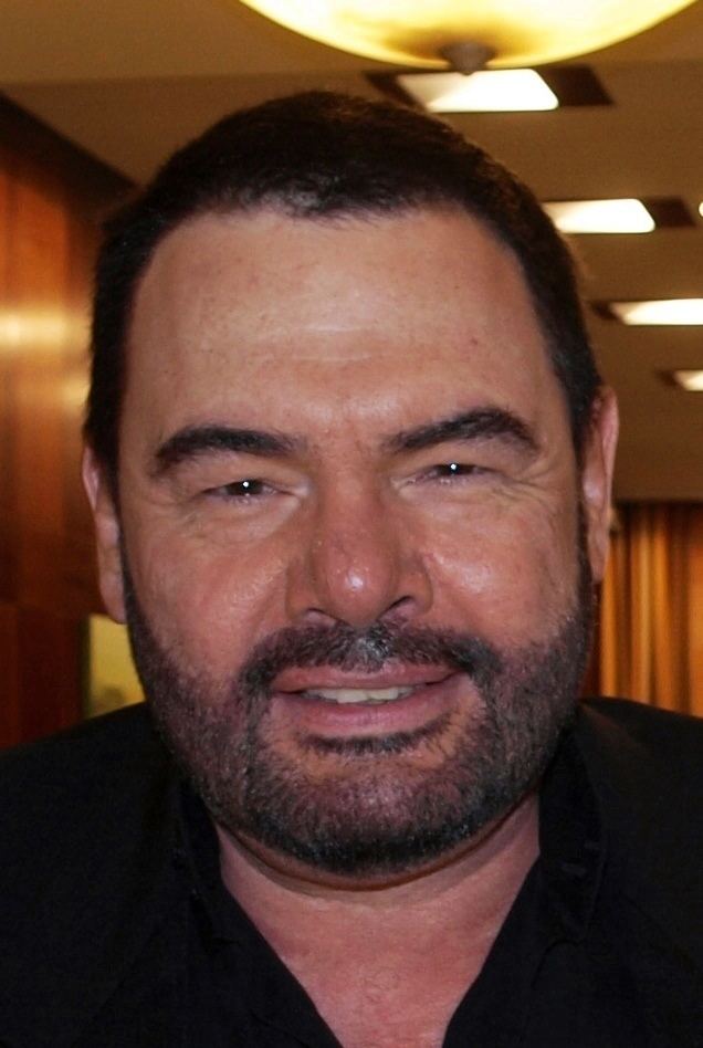 Marian Gold smiling, with a beard and mustache and wearing a black shirt.
