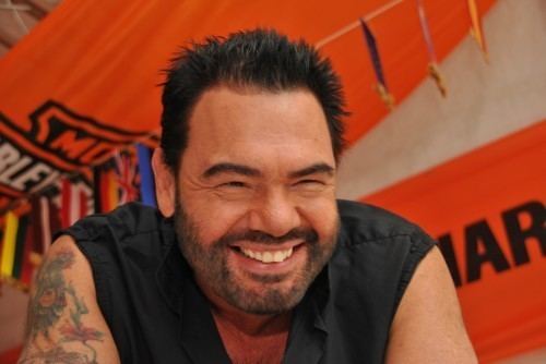 Marian Gold smiling, with a beard and mustache and wearing a black sleeveless shirt.