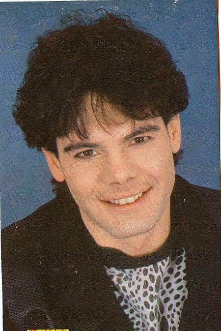 Marian Gold smiling and wearing a black suit and a black and white shirt.