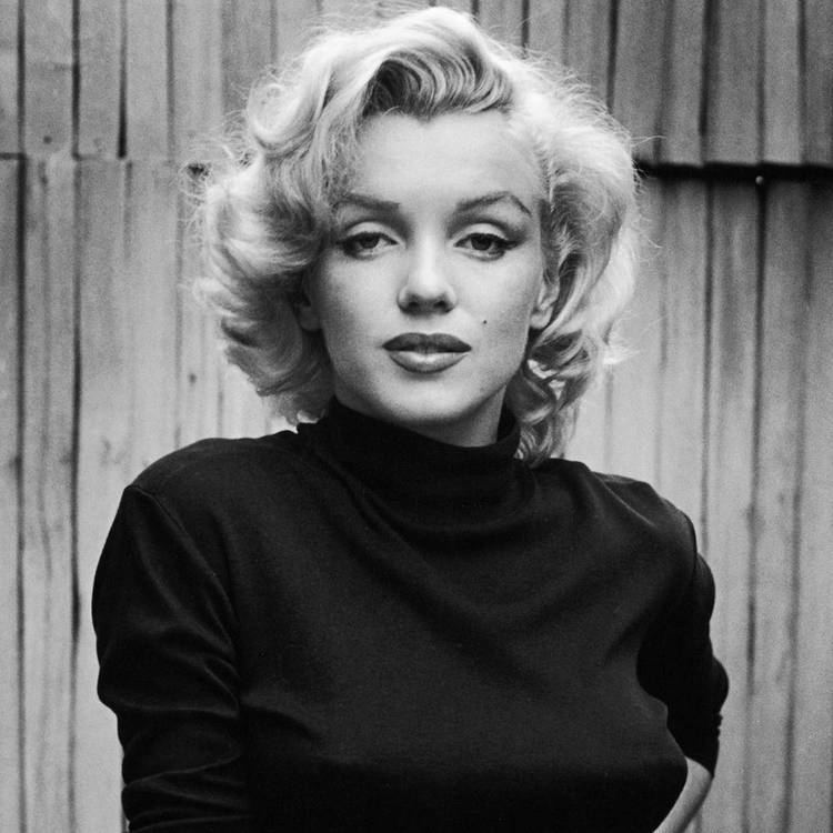 Marilyn Monroe is serious, has white hair, a mole on her left cheek, wearing a black turtle neck top.