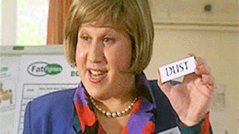 Marjorie Dawes in Little Britain-Fight Fighters, smiling while holding a piece of paper, with short blonde hair, wearing a necklace, and a blue blazer over a multi-colored polo shirt.