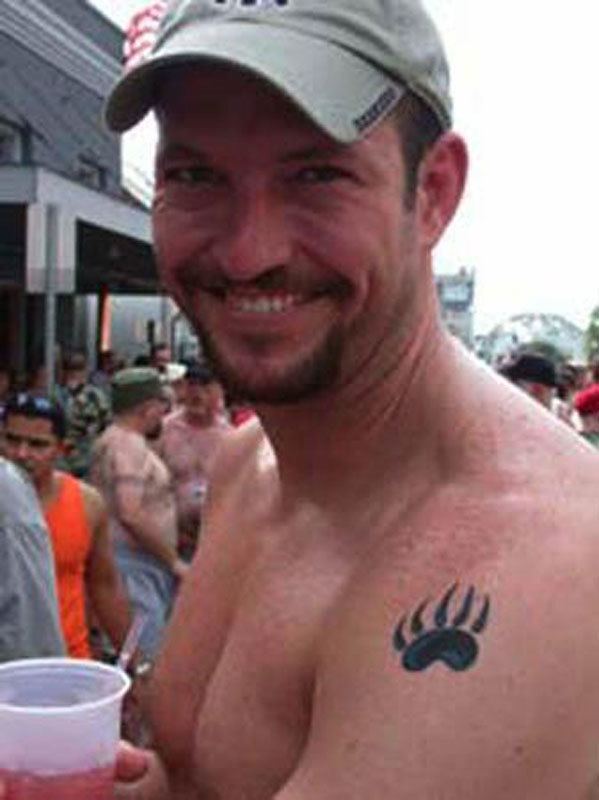 Mark Bingham smiling while holding a cup of juice and wearing a gray cap