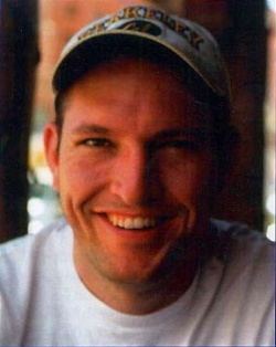 Mark Bingham smiling while wearing a cap and white t-shirt