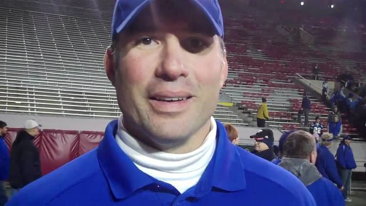 Mark Chmura wearing blue cap, white turtle neck and blue polo shirt at Camp Randall Stadium