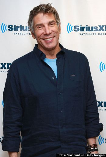 Mark Goodman smiling while wearing dark blue long sleeves, blue inner shirt, and bracelets