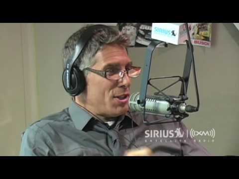 Mark Goodman telling a story about Michael Jackson while wearing a headphone, gray long sleeves, and eyeglasses