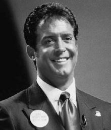 Mark R. Hughes smiling on stage and wearing a suit and tie.