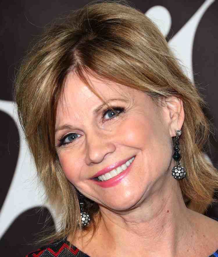 Markie Post smiling and wearing a colored blouse and black dangling earrings
