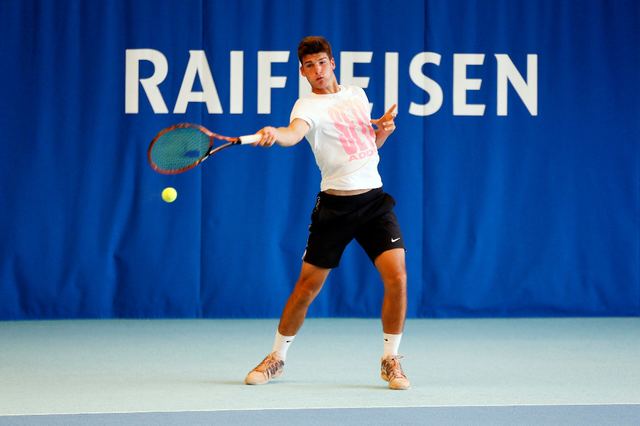 Marko Osmakcic playing tennis while wearing a white and pink t-shirt, black shorts, white socks, and rubber shoes