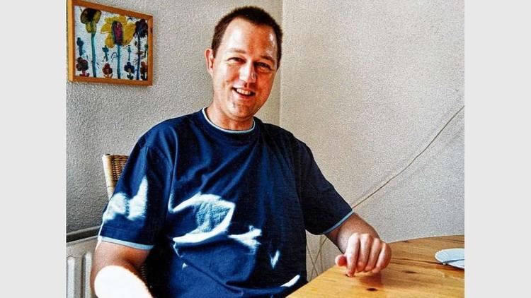 Martin Ney smiling inside his house and wearing a blue shirt.