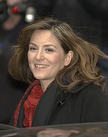 Martina Gedeck smiling while wearing a black blouse and black and red scarf