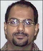 Marwan al-Shehhi smiling with a mustache and beard while wearing a red and white checkered shirt and eyeglasses