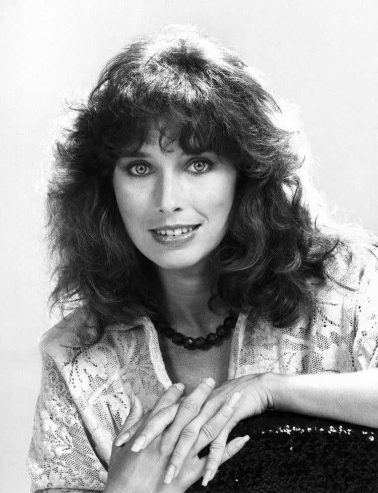 Mary Kate McGeehan smiling with wavy hair and interlocking fingers while wearing a lace blouse and necklace