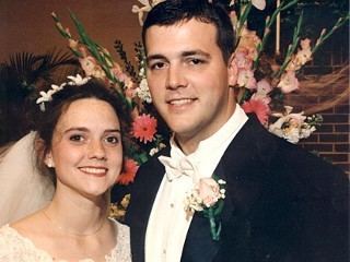 Mary and Matthew Winkler are smiling at their wedding. Mary wearing a white gown while Matthew wearing a black coat over white long sleeves.