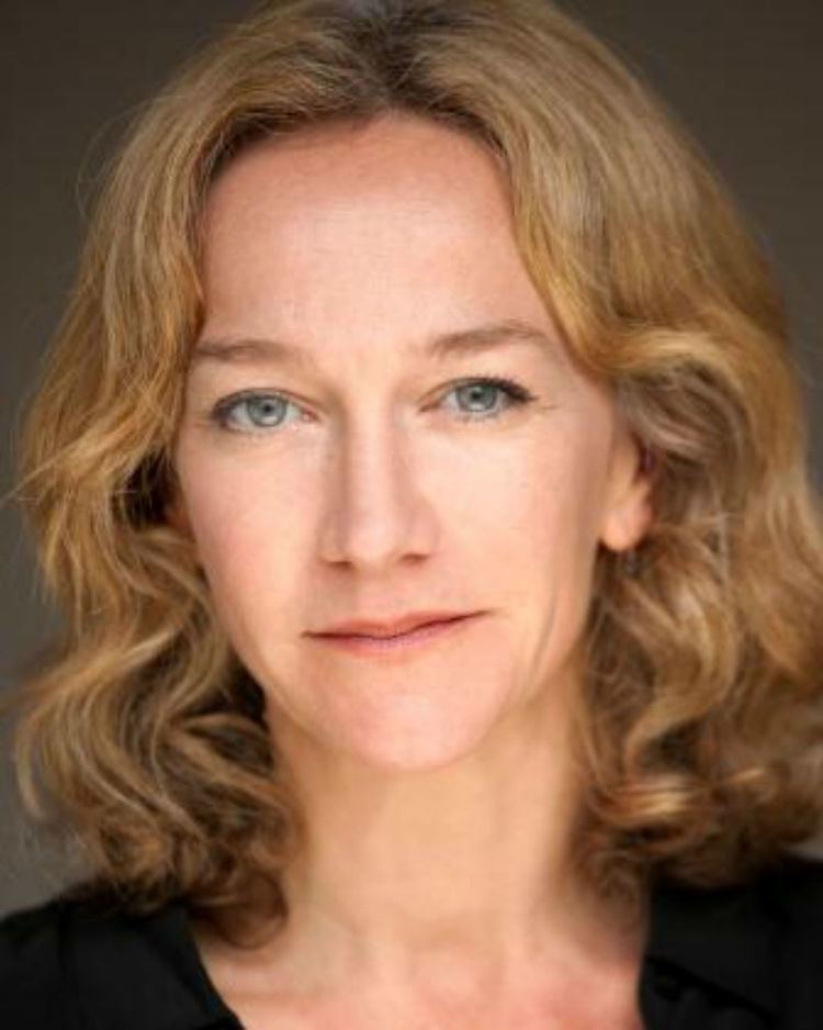 Matilda Ziegler with a tight-lipped smile and curly hair while wearing a black blouse