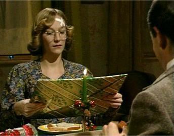 Matilda Ziegler as Irma Gobb in the 1990 tv series, Mr. Bean while holding a gift and wearing eyeglasses and brown and blue dress