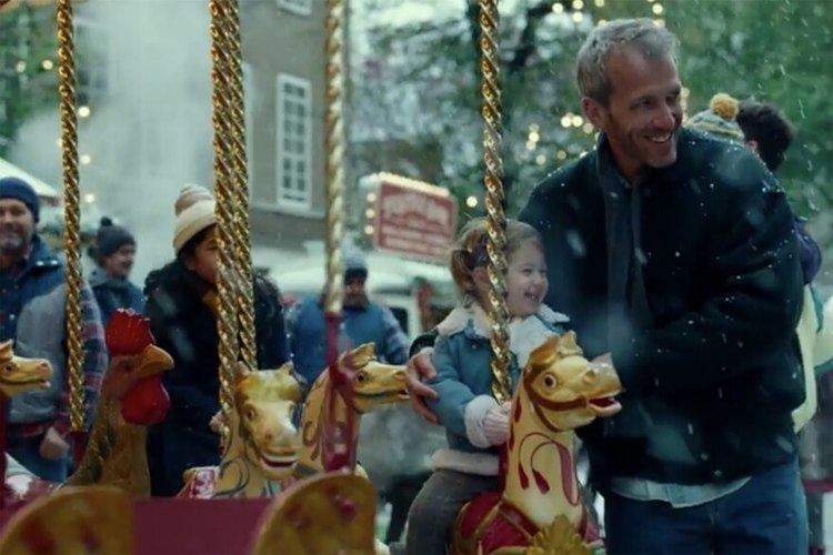 Maya Versano riding in a Carousel and looking very happy while being held by her father, Yaron Versano in a blue coat