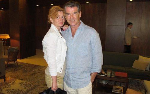 Mediha Musliovic posing with Pierce Brosnan and wearing a white dress and carrying a black bag.