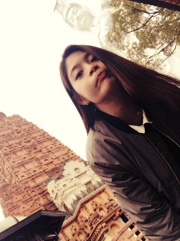 Megu Fujiura posing near the ancient building and the Buddha statue while wearing a black jacket