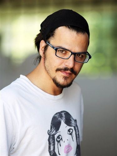 Mehmet Günsür posing and wearing a black beanie and a white shirt as well as eyeglasses.