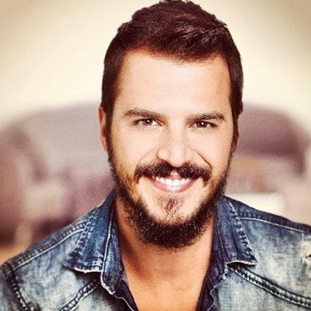 Mehmet Gunsur smiling with thick facial hair and wearing a blue jean jacket.