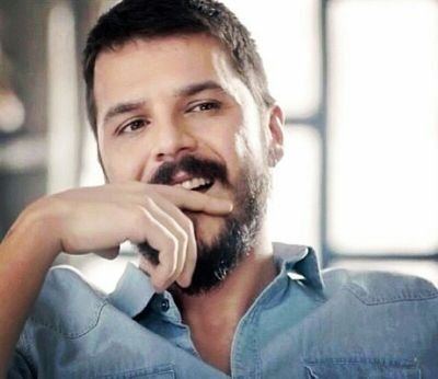 Mehmet Günsür laughing with his hand on his face and wearing a casual jean shirt.