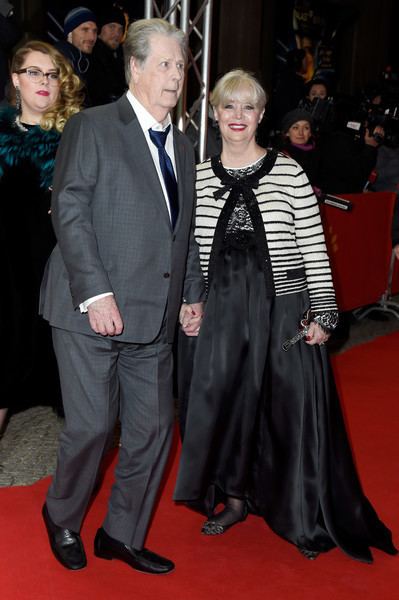 Melinda Ledbetter with short blonde hair, wearing black earrings and a white and black dress with Brian Wilson wearing a suit, a blue tie, and black shoes on a red carpet.