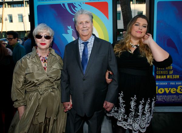 Melinda Ledbetter with short blonde hair, wearing sunglasses, a necklace, and a green dress with Brian Wilson wearing a suit and a blue tie together with Carnie Wilson wearing a necklace and a black dress.