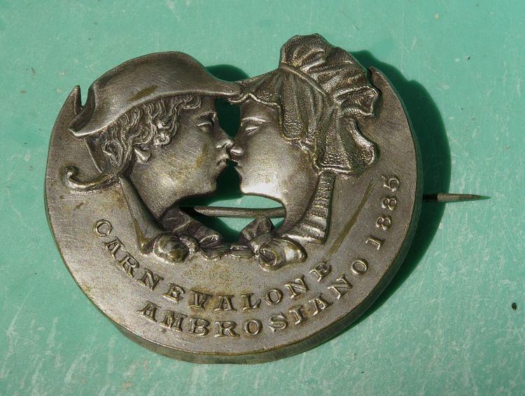 A pin with a carved image of Meneghino and Cecca and words written "CARNEVALONE AMBROSIANO 1885"
