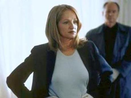 Ellen Barkin standing with hands on her hips and wearing a white blouse and black coat in a scene from the 2000 movie "Mercy"