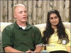 Meriam Al-Khalifa sitting on the couch and wearing a yellow blouse while Jason Johnson wearing a green polo shirt