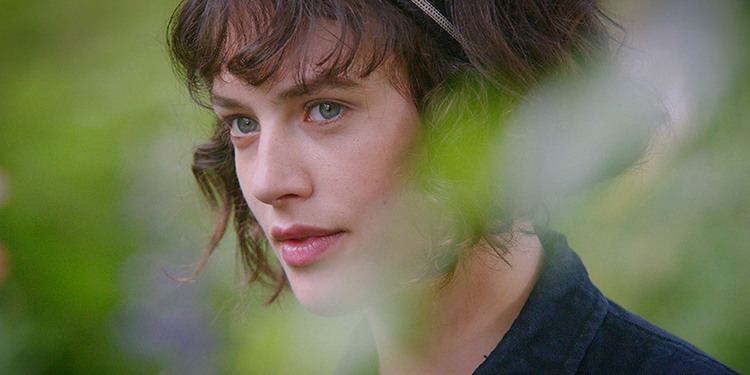 Jessica Brown Findlay looking at something while wearing a black blouse in a scene from the 2016 film, This Beautiful Fantastic