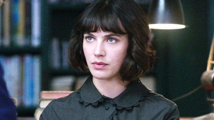 Jessica Brown Findlay looking at someone while at the library and wearing a black dress in a scene from the 2016 film, This Beautiful Fantastic