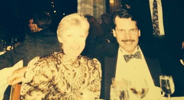 A photo of a woman with a man in a party, sitting on a table with wine glass.